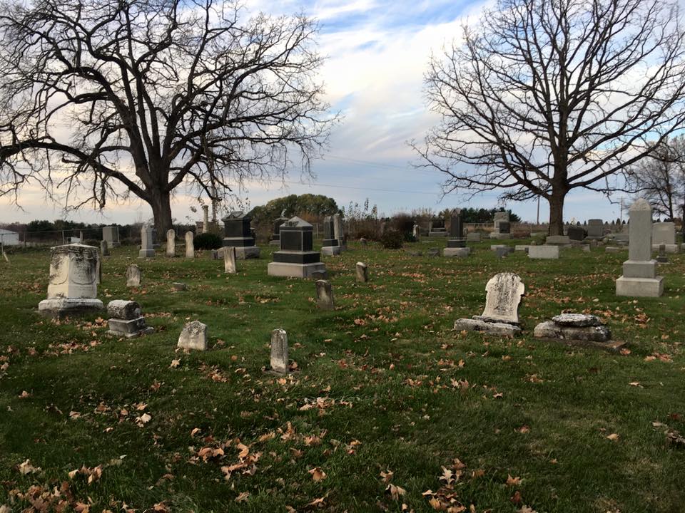 Wide view of cemetery grounds with mature trees and memorial markers.